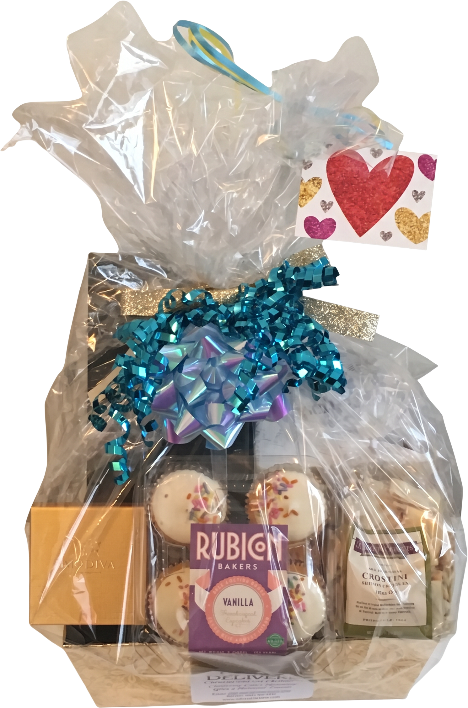 Cellophane-wrapped gift basket with a teal bow, Godiva chocolates, cupcakes, and a heart gift tag